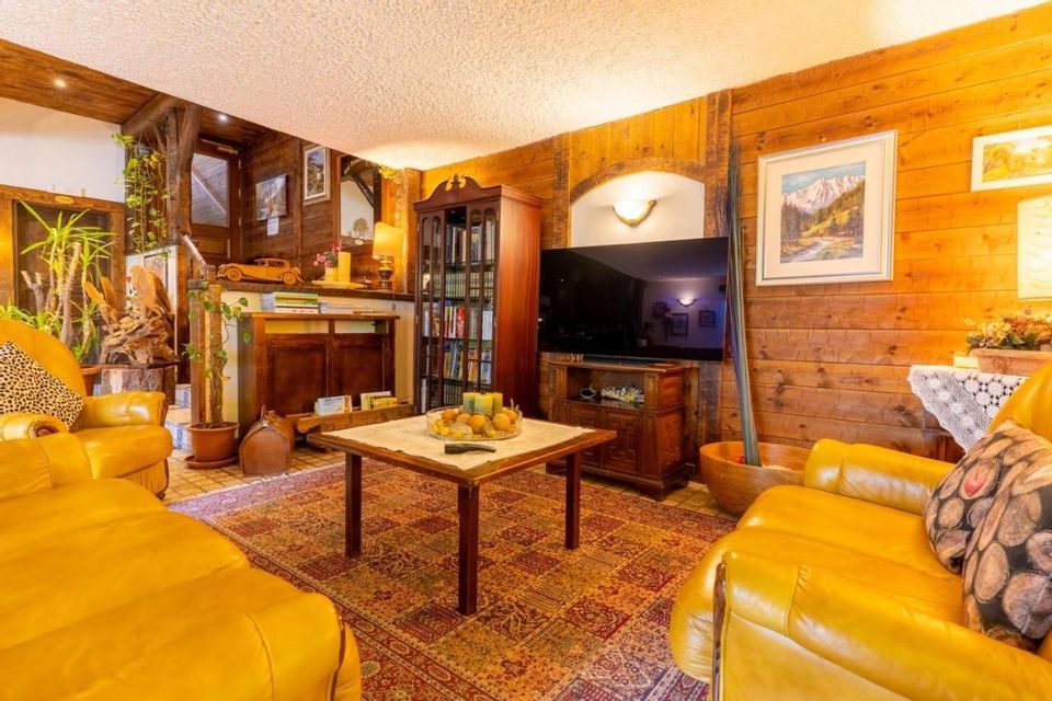 Soggiorno rustico con divani in pelle gialli, pareti in legno, tavolino da caffè su tappeto fantasia e televisore.