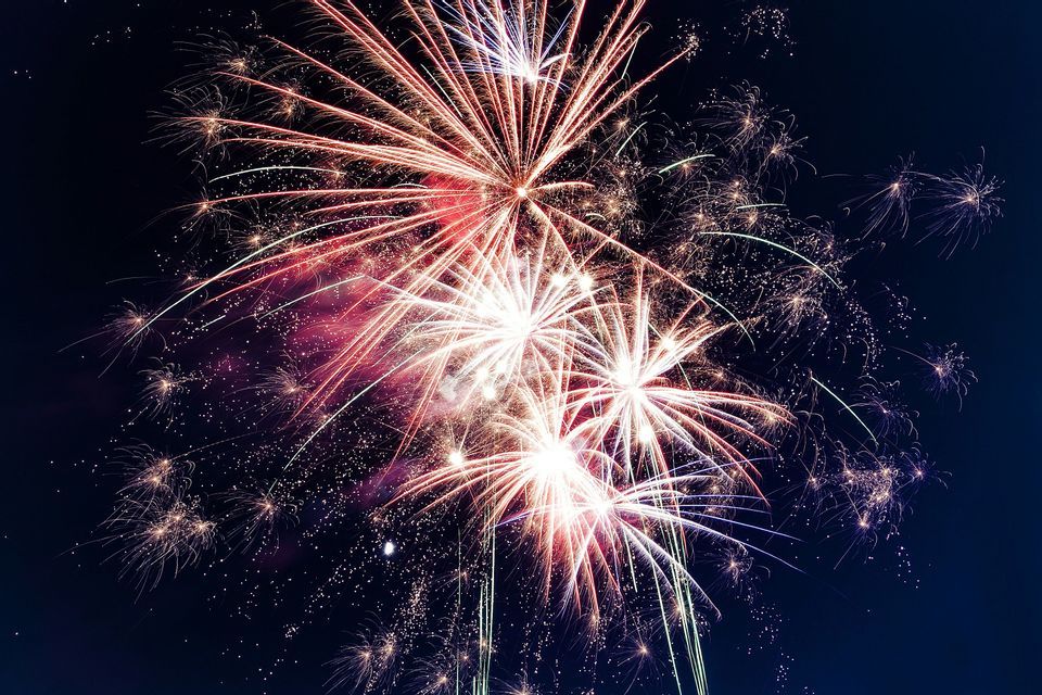 Fuochi d'artificio rossi e bianchi esplodono in luminosi bagliori contro il cielo notturno scuro.