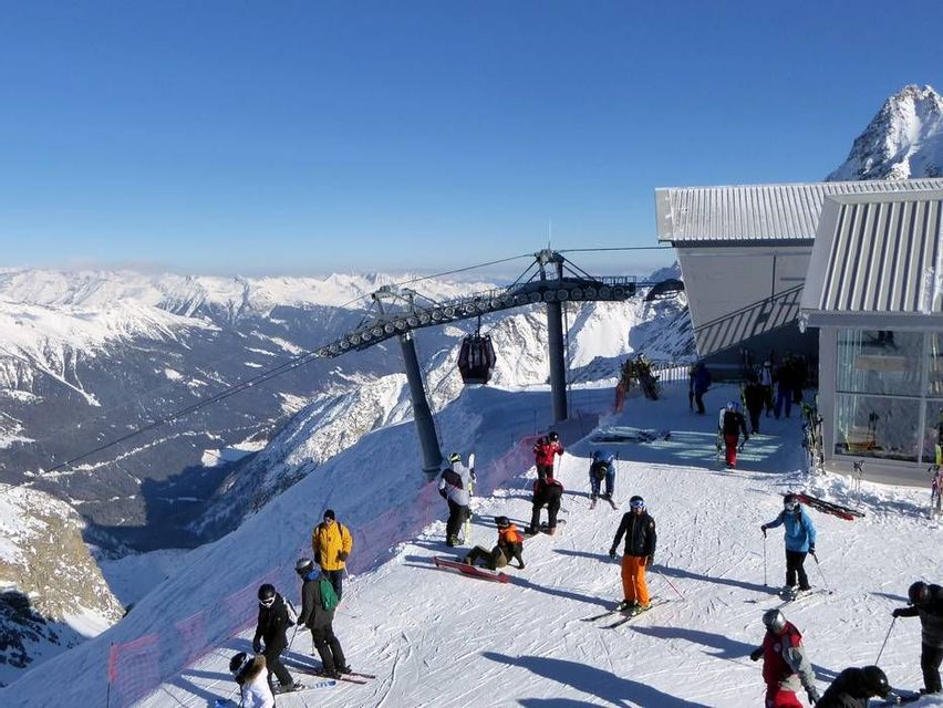 Un viaggio di gruppo WeRoad per sciare su una cima di montagna assolata, con funivia e cime innevate sullo sfondo.