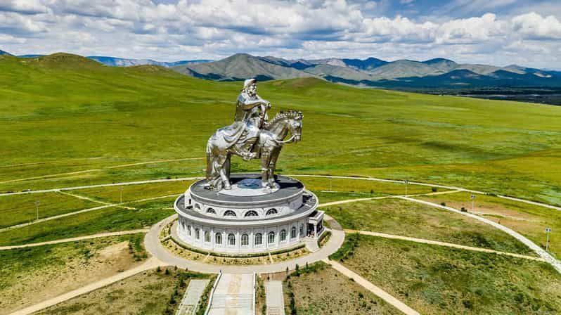 Una veduta aerea di una gigantesca statua equestre argentata in cima a un edificio circolare, sullo sfondo di verdi colline ondulate e montagne.