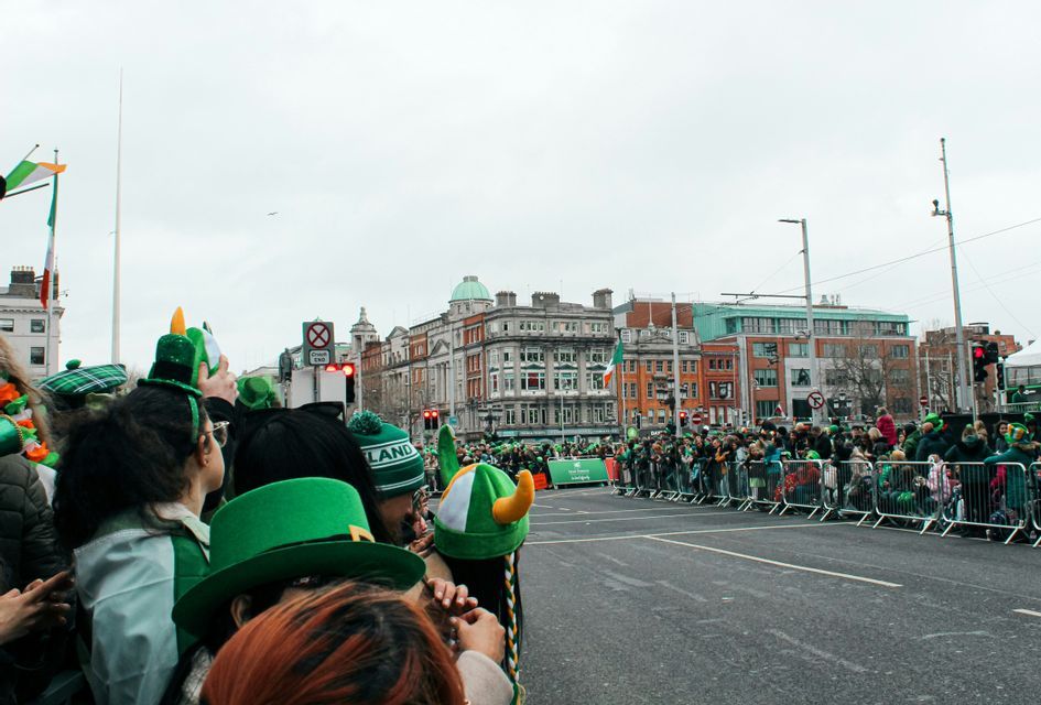 Un voyage de groupe WeRoad observe un défilé derrière des barricades, avec de nombreuses personnes portant des chapeaux verts.