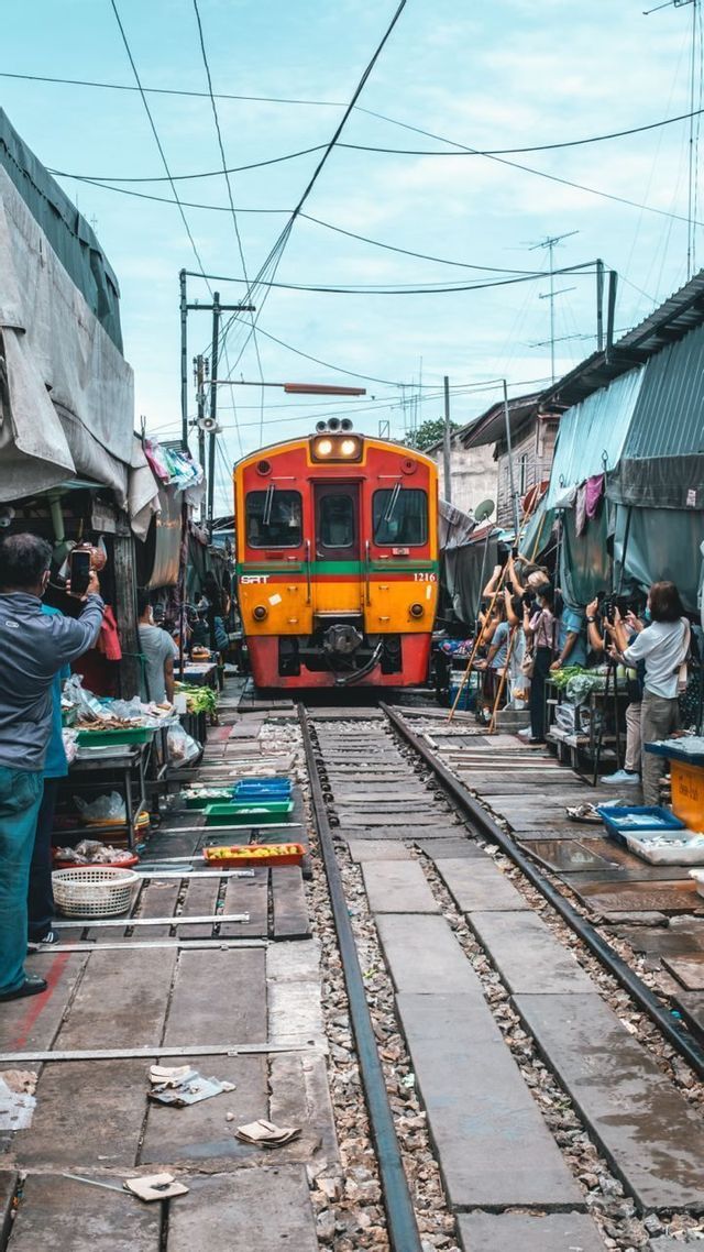 Un tren rojo y amarillo se mueve lentamente por un mercado estrecho mientras la gente de un viaje en grupo de WeRoad toma fotos.