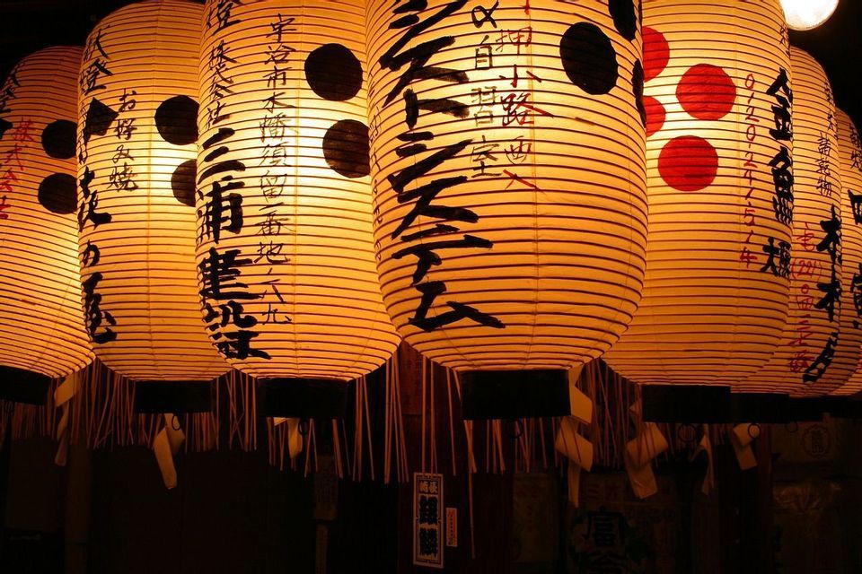 Una fila di lanterne di carta giapponesi illuminate con calligrafia pende nell'oscurità, proiettando un caldo bagliore.
