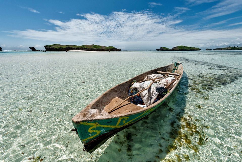 Ein grünes Holzkanu mit Angelausrüstung schwimmt in flachem, kristallklarem Wasser, mit kleinen Inseln am Horizont unter blauem Himmel.