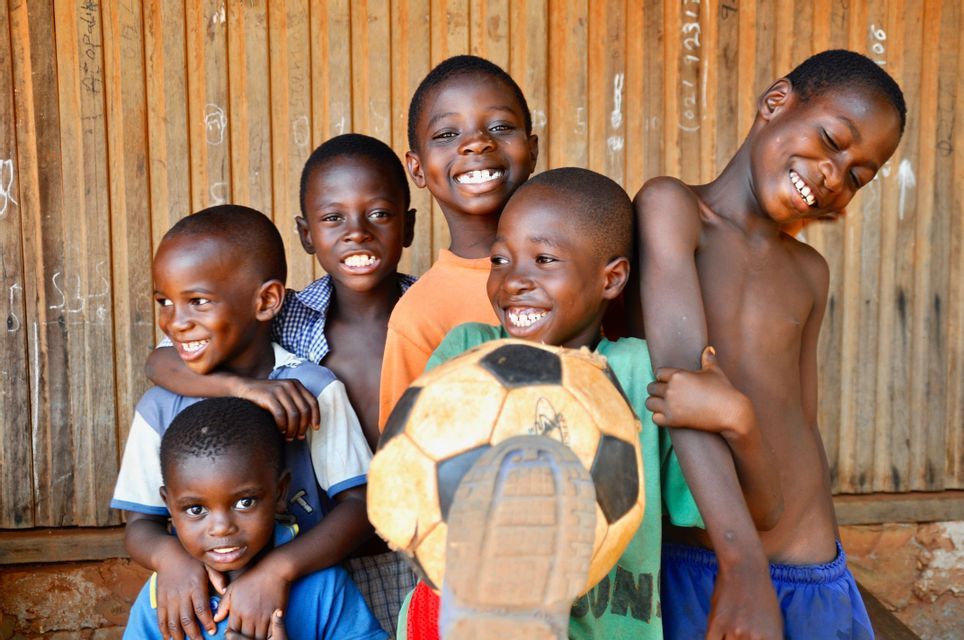 Seis niños sonriendo y riendo juntos, posando con un balón de fútbol frente a una pared de madera.