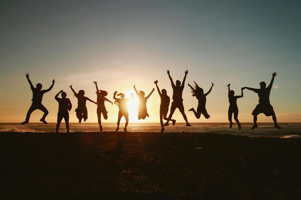 Un viaggio di gruppo WeRoad con persone in silhouette che saltano su una spiaggia al tramonto.