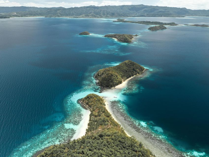 Vista aerea di piccole isole verdi con spiagge di sabbia bianca, circondate da acque oceaniche turchesi e blu profondo.