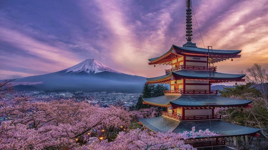 Una pagoda rossa si erge tra ciliegi in fiore, con vista su una città e una montagna innevata sullo sfondo sotto un cielo viola.