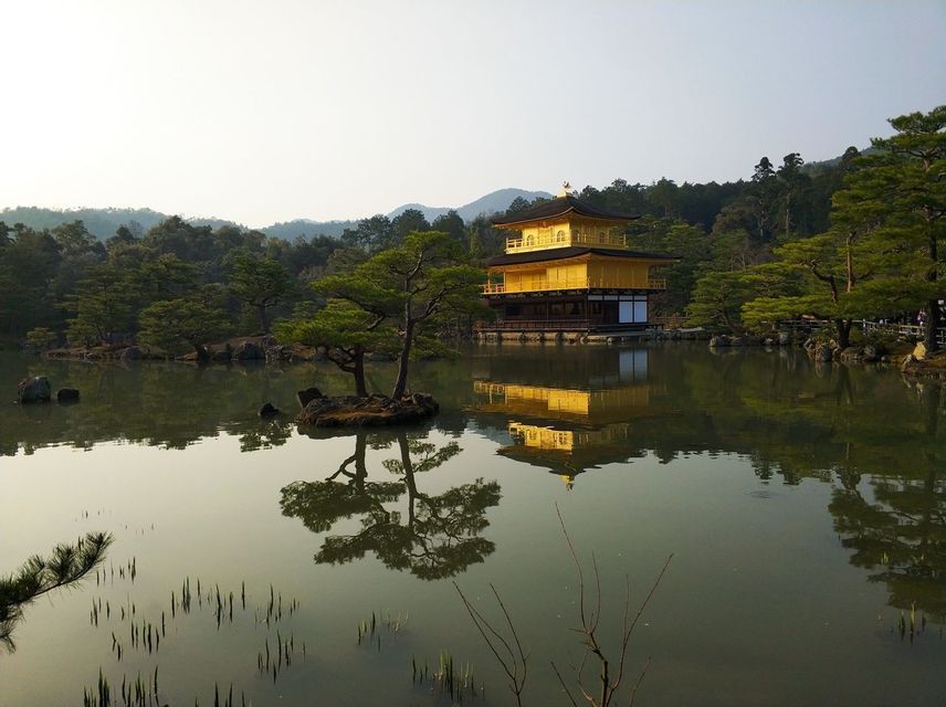 Un tempio dorato a più livelli si erge accanto a un lago calmo, con il suo riflesso visibile sulla superficie dell'acqua vicino a una piccola isola.