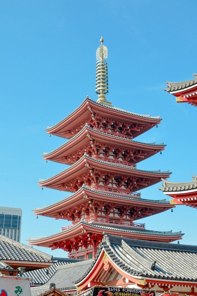 Una pagoda alta, rossa, a cinque piani con un ornato pinnacolo dorato si staglia contro un cielo limpido e azzurro brillante.