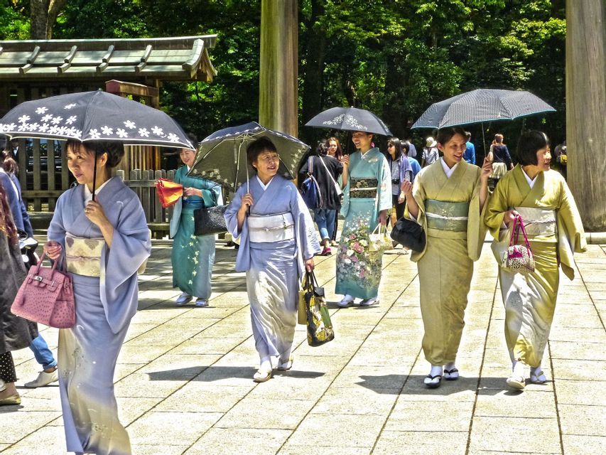 Un gruppo di donne giapponesi in kimono colorati cammina su un sentiero lastricato, tenendo ombrelli aperti per l'ombra.