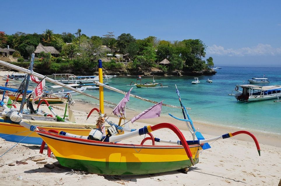 Barche tradizionali colorate ormeggiate su una spiaggia di sabbia, accanto a una tranquilla baia turchese e a una costa verde.
