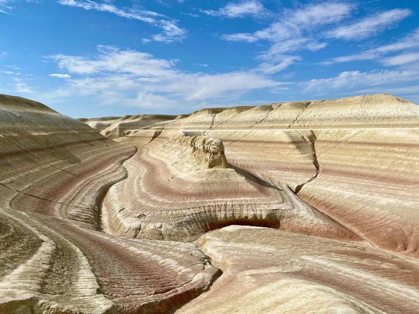 Coloridas formaciones rocosas estratificadas de sedimento rojo y blanco forman colinas ondulantes en un cañón bajo un cielo azul.