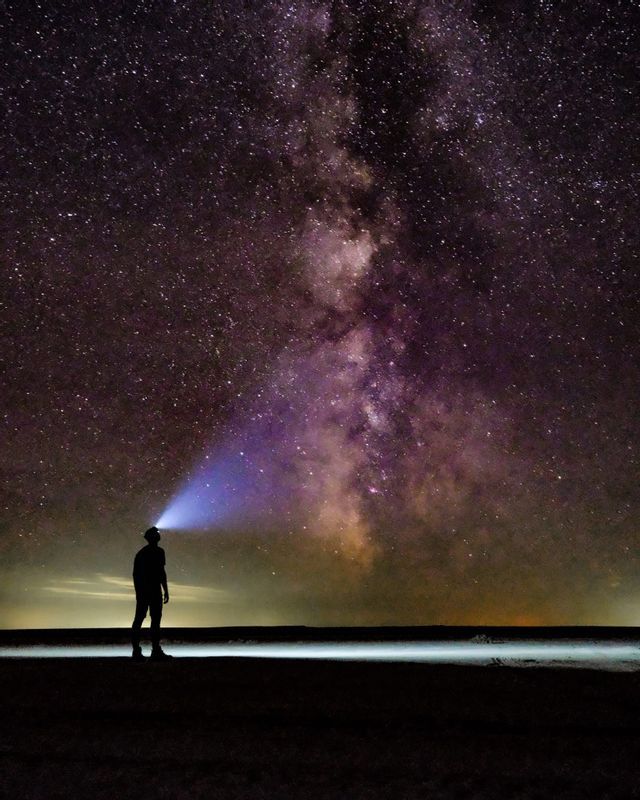 Una persona in silhouette con una lampada frontale guarda la Via Lattea sotto un vasto cielo notturno stellato.