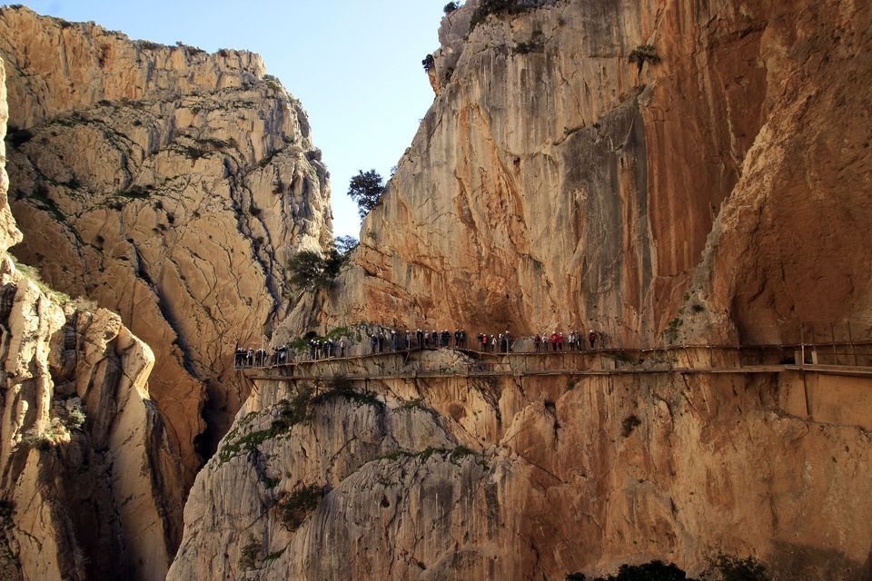 Un viaggio di gruppo WeRoad cammina in fila indiana lungo una stretta passerella attaccata alla parete rocciosa a strapiombo di un grande canyon.