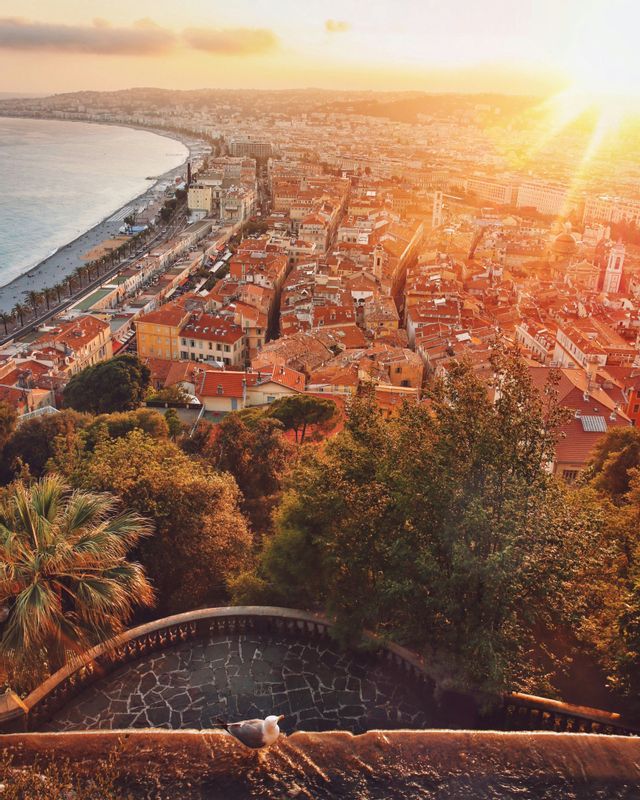 Vue aérienne d'une ville côtière aux toits rouges et d'une longue plage, baignée par la lumière chaude d'un soleil couchant.
