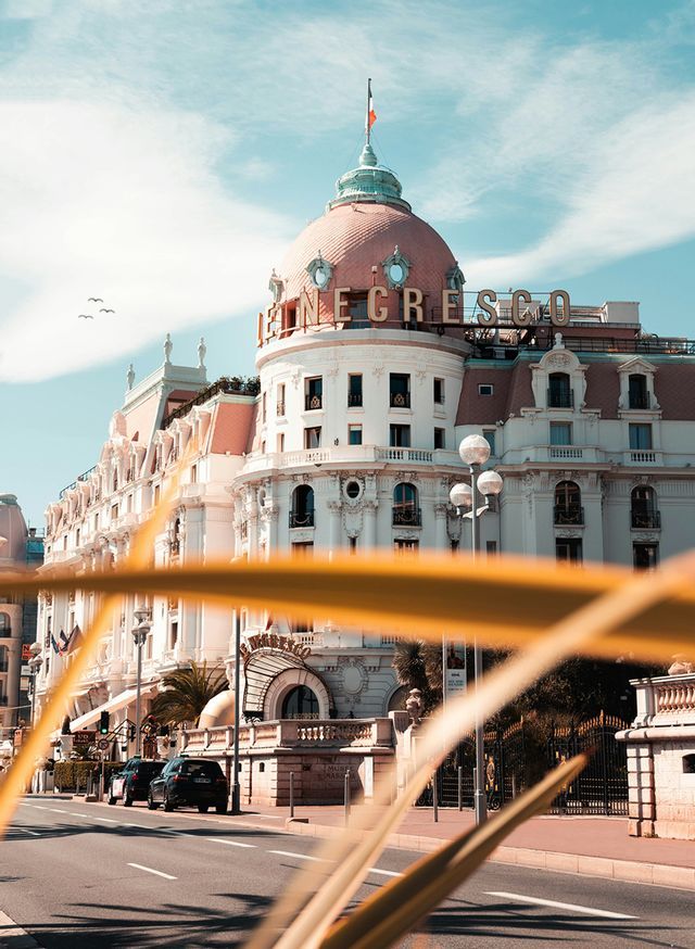 L'hôtel Le Negresco, avec son dôme rose emblématique, vu depuis une rue par une journée ensoleillée.