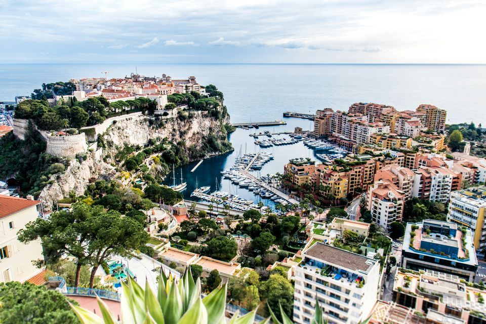 Vue plongeante sur une ville côtière bâtie sur une falaise rocheuse, avec un port rempli de yachts et de bateaux en contrebas.