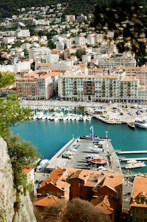Une vue plongeante du port d'une ville côtière, rempli de voiliers amarrés et adossé à des bâtiments à flanc de colline.