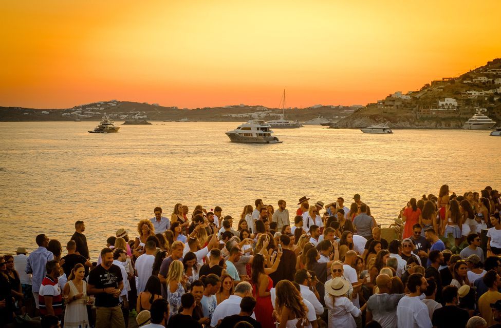 Un viaggio di gruppo WeRoad si riunisce in riva al mare al tramonto, con yacht sull'acqua e una costa sullo sfondo.