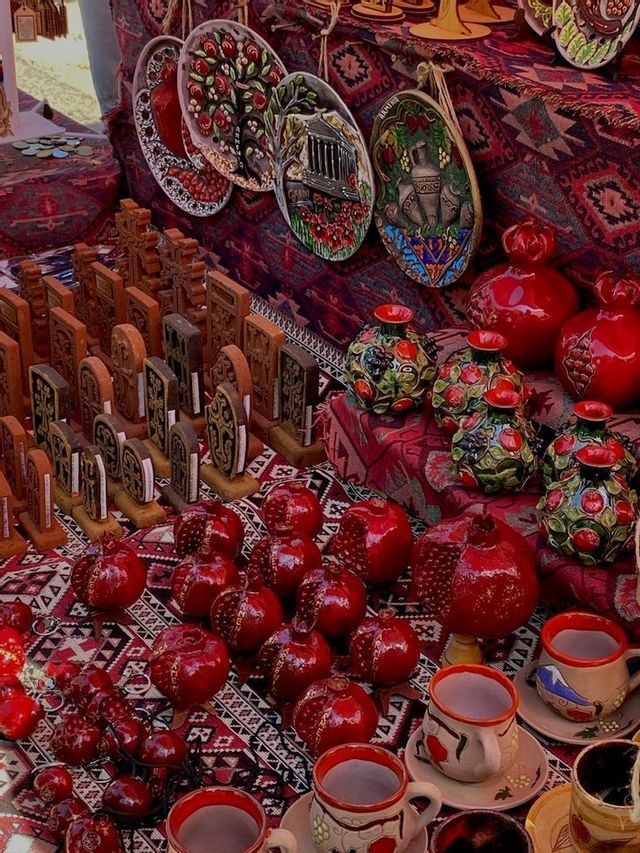 Souvenir in ceramica artigianale, incluse melagrane, vasi e targhe, esposti su un tessuto rosso a fantasia in un mercato.