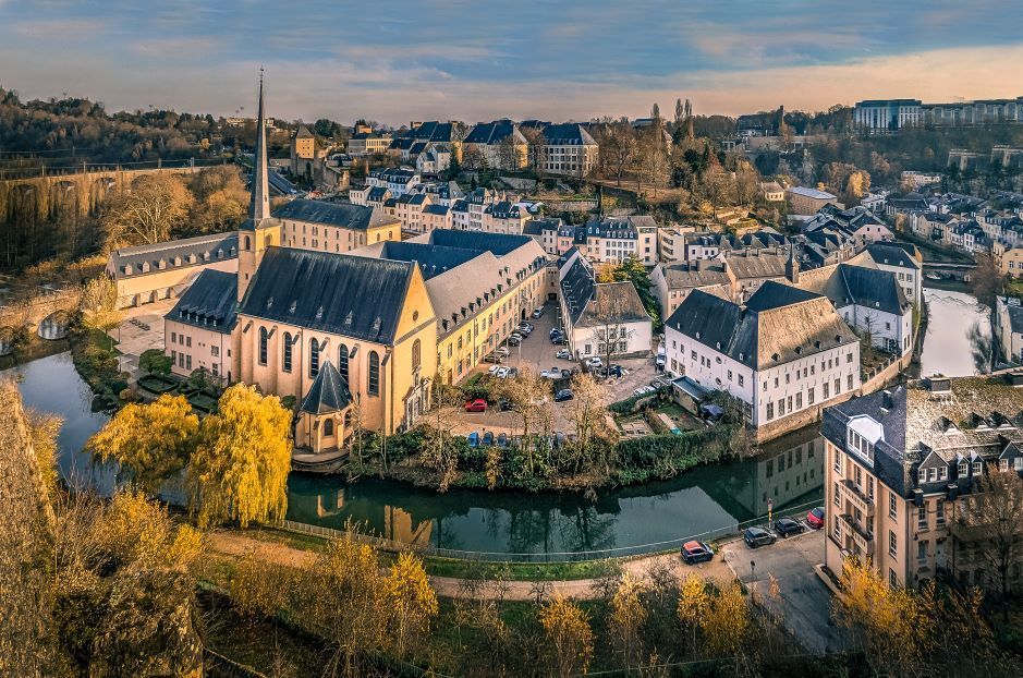Veduta aerea di una città storica con una chiesa e la sua guglia ben visibili, adagiata nell'ansa di un fiume in autunno.