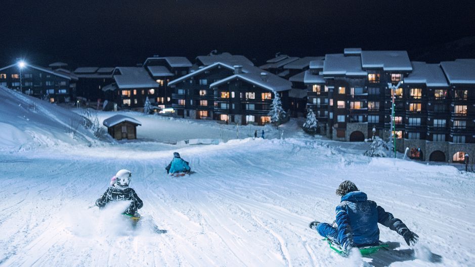 Un viaggio di gruppo WeRoad che slitta giù per un pendio innevato di notte, con chalet illuminati sullo sfondo.