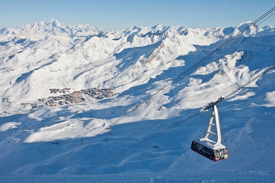 Una funivia viaggia in alto sopra una vasta valle montana innevata con una piccola località sciistica in lontananza.