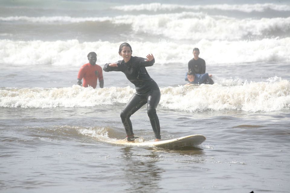 Una donna in muta nera di un viaggio di gruppo WeRoad sorride mentre impara a bilanciarsi su una tavola da surf tra le onde dell'oceano.