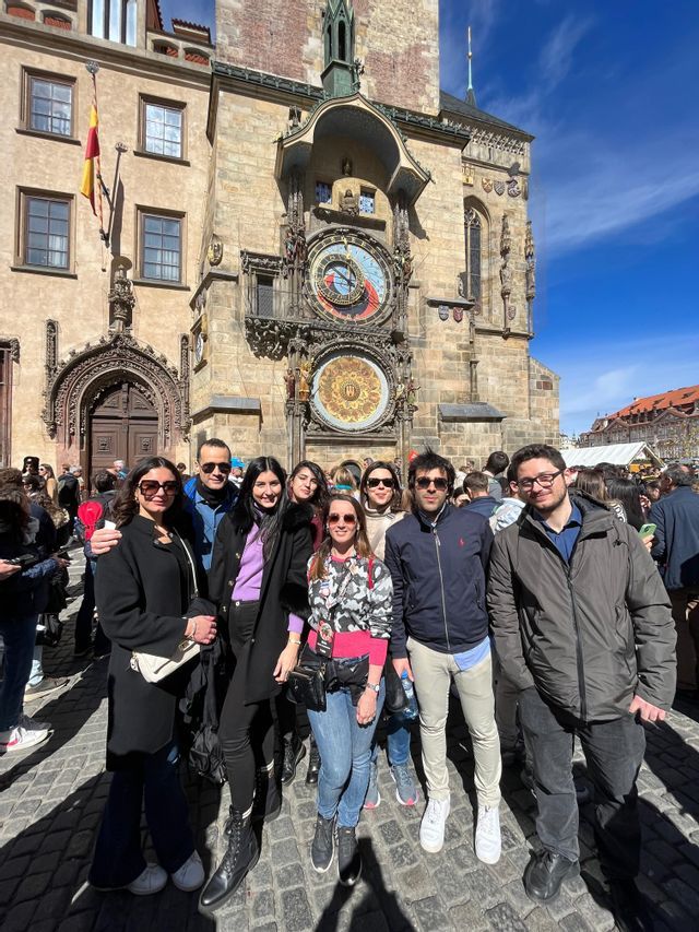 Eine WeRoad-Gruppenreise posiert für ein Foto auf einem sonnigen Stadtplatz vor einem historischen astronomischen Uhrturm.