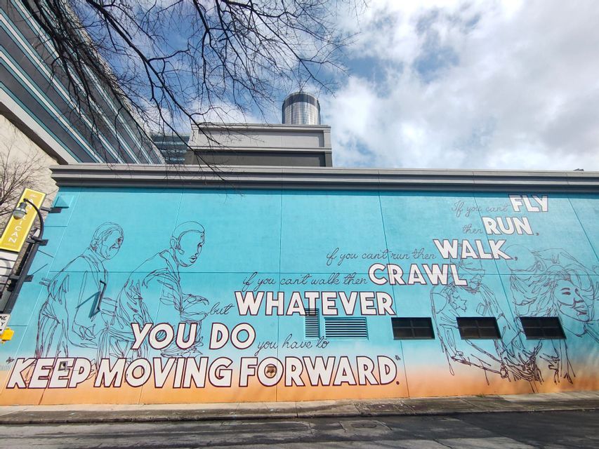 Un grande murale blu e arancione sul lato di un edificio con la citazione motivazionale 'Continua ad andare avanti'.
