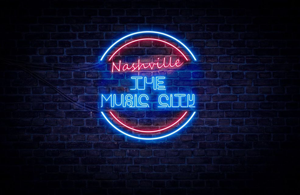Un'insegna al neon rossa e blu con la scritta 'Nashville The Music City' che brilla su un muro di mattoni scuri.