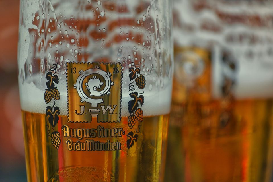 Primo piano di un bicchiere di birra Augustiner-Bräu München, con schiuma densa e goccioline di condensa.