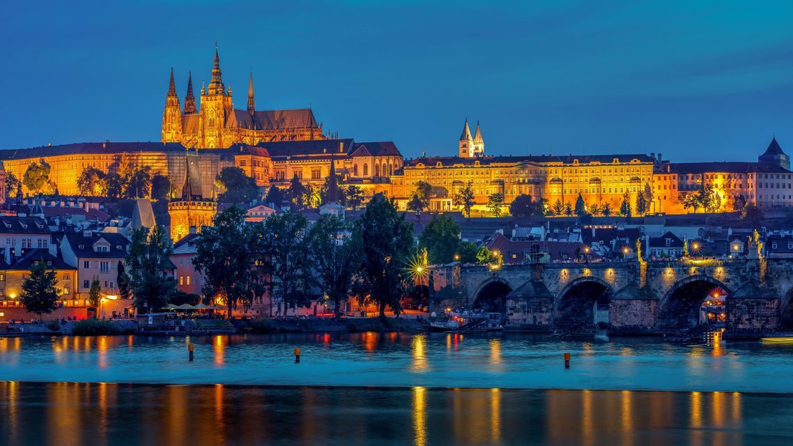 Prague Castle and Charles Bridge lit up at night above the Vltava river.