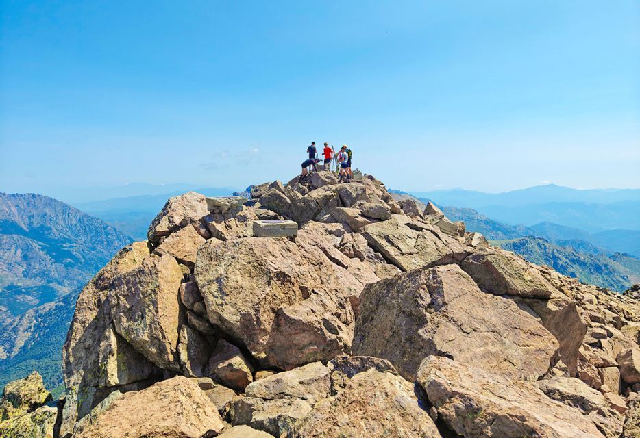 Un voyage de groupe WeRoad se tient sur un sommet rocheux, surplombant une vaste chaîne de montagnes sous un ciel bleu clair.