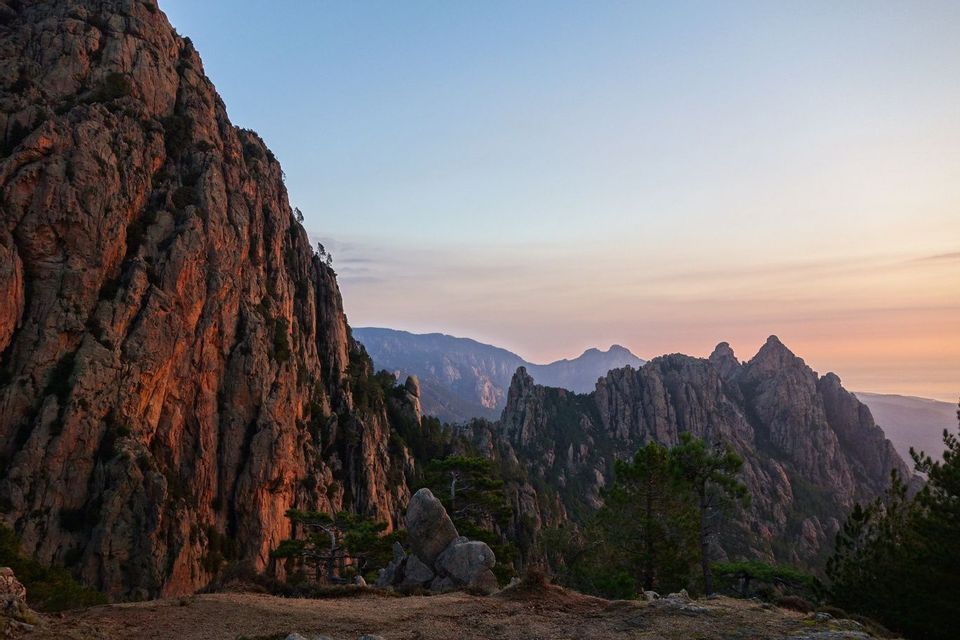 Une chaîne de montagnes accidentée avec des sommets déchiquetés, baignée par la lumière chaude du lever du soleil sous un ciel dégagé.