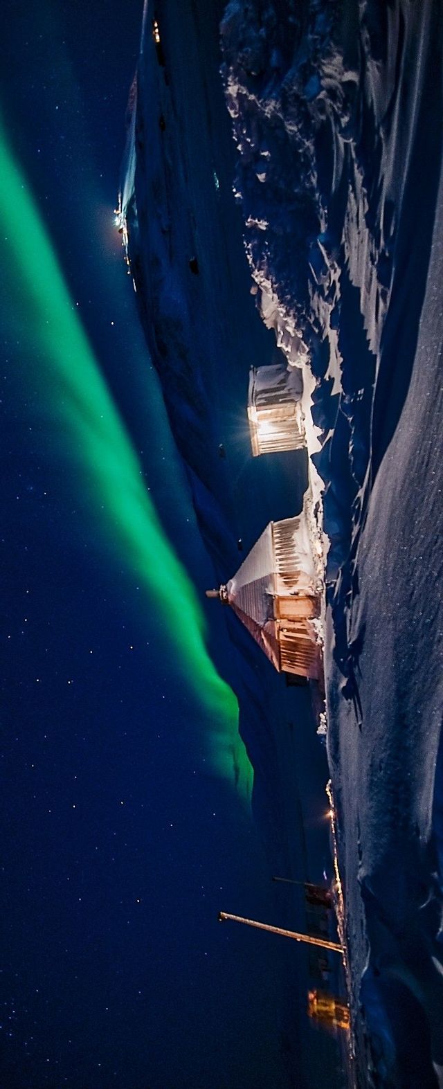 Uno scatto verticale dell'Aurora Boreale verde su baite innevate in montagna, sotto un cielo stellato.