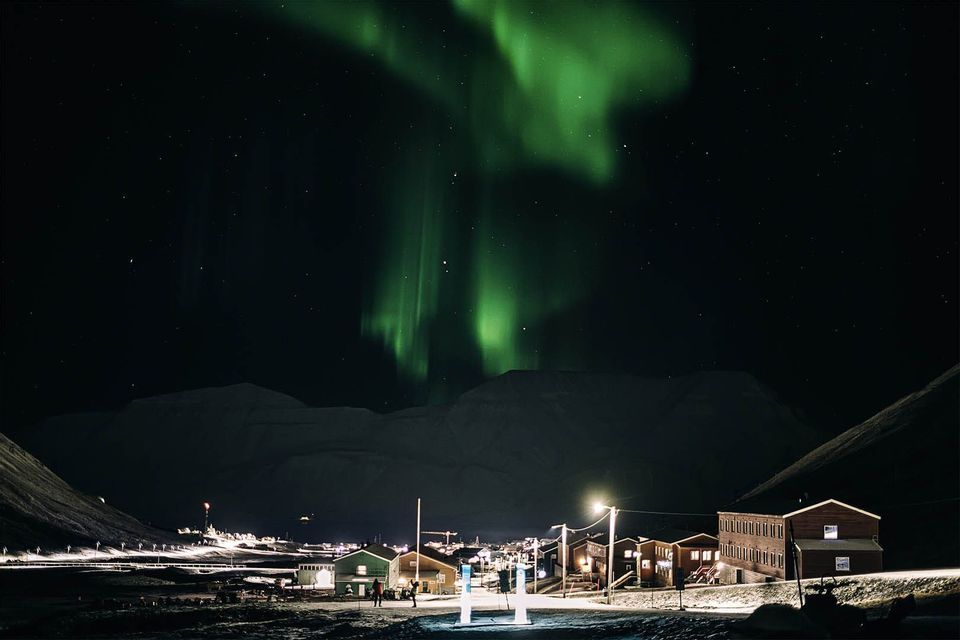 L'aurora boreale verde risplende nel cielo notturno scuro sopra una città illuminata coperta di neve alla base delle montagne.