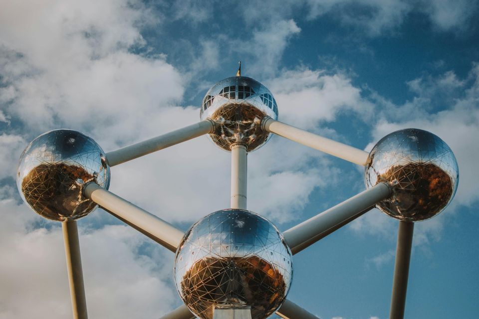 Un monument avec de grandes sphères réfléchissantes connectées par des tubes, vu d'en bas contre un ciel bleu avec des nuages blancs.