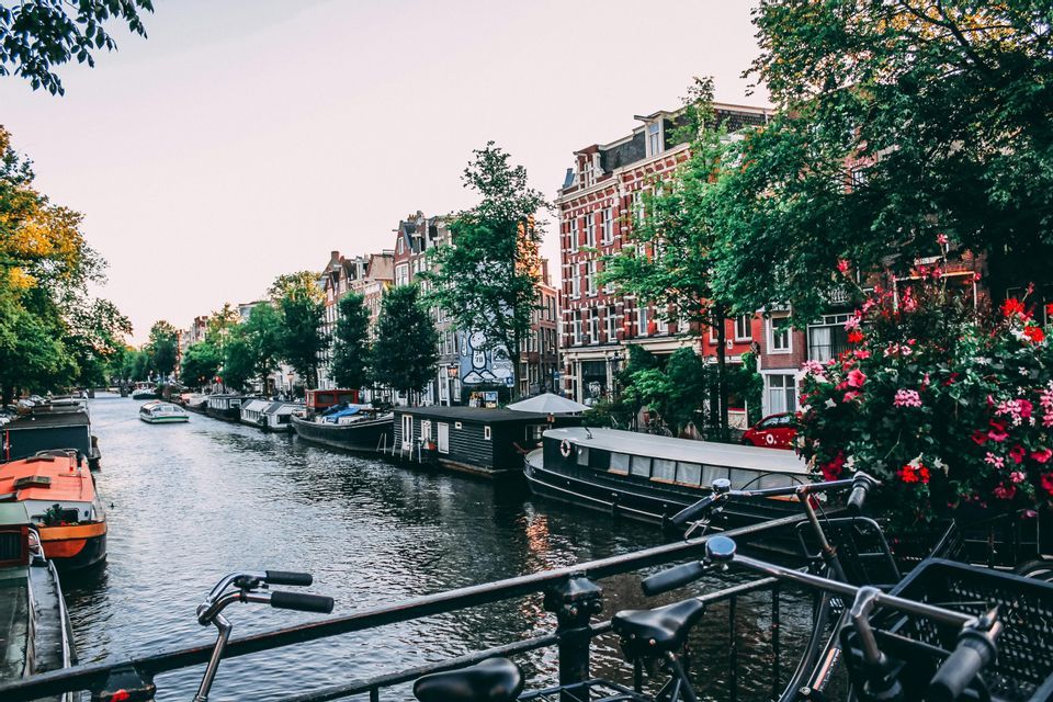 Des vélos garés sur un pont surplombant un canal de ville bordé de péniches, d'arbres et de bâtiments traditionnels.