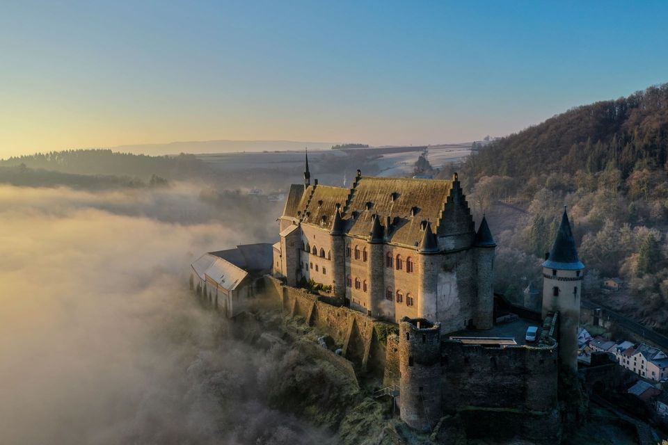 Una veduta aerea di un grande castello in pietra su una collina, che si erge sopra una coltre di nebbia all'alba.