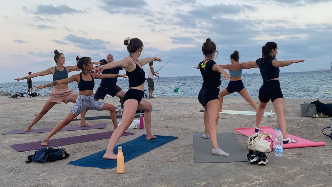 Eine WeRoad-Gruppenreise, die eine Yoga-Pose auf Matten auf einem Betonsteg am Meer unter bewölktem Himmel übt.