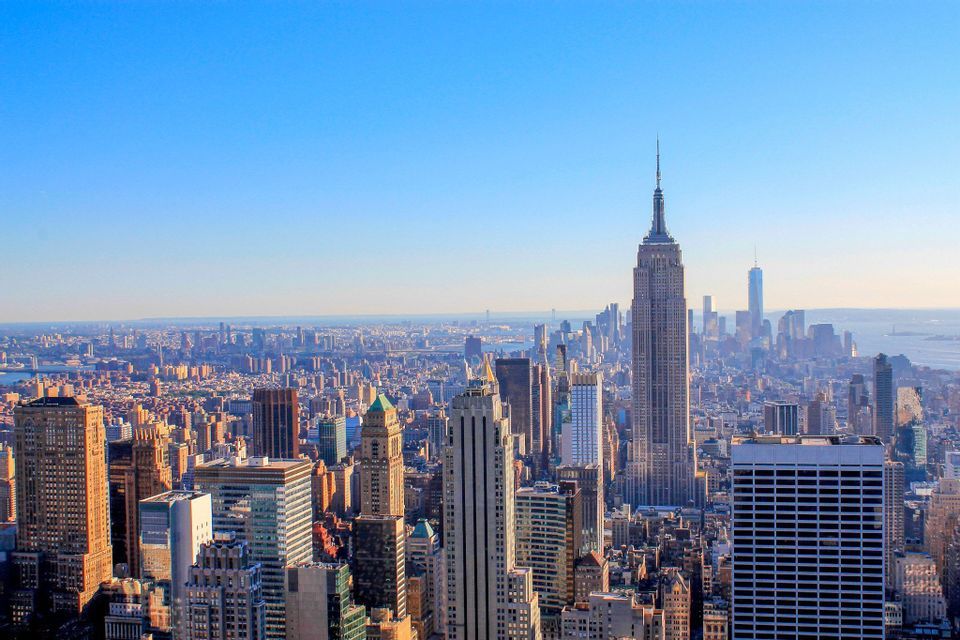An aerial view of the New York City skyline, with the Empire State Building prominently featured under a clear blue sky.