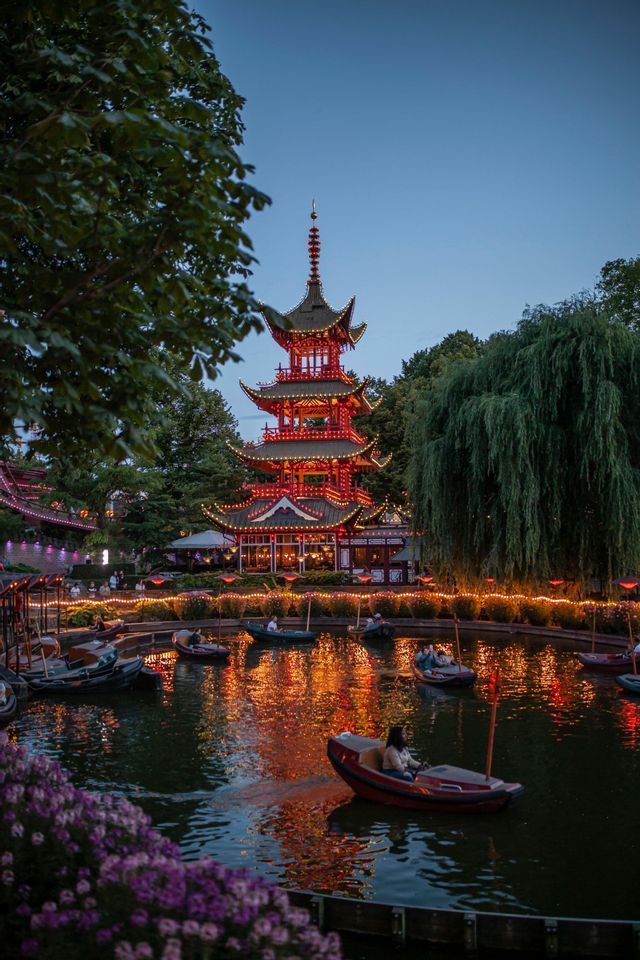 Una grande pagoda rossa è illuminata al crepuscolo, le sue luci si riflettono su uno stagno dove le persone vanno in piccole barche.