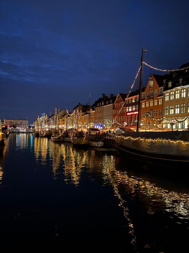 Barche e edifici colorati decorati con luci festive costeggiano un canale di notte, con i loro riflessi che brillano sull'acqua.