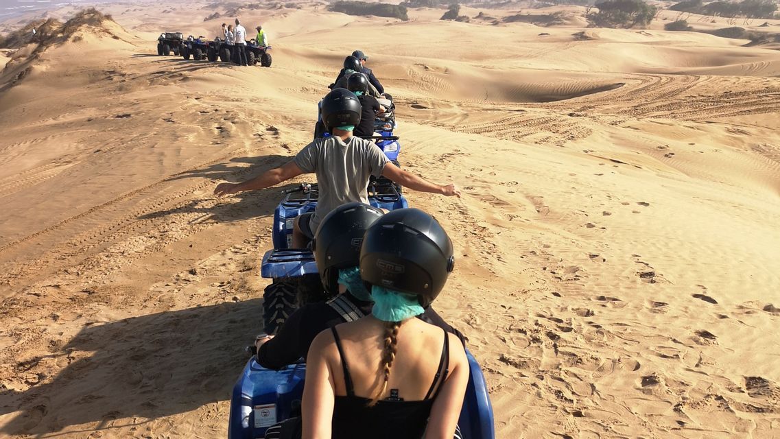 Eine WeRoad Gruppenreise, bei der ATVs in einer Reihe weite Wüstendünen durchqueren, von hinten gesehen.