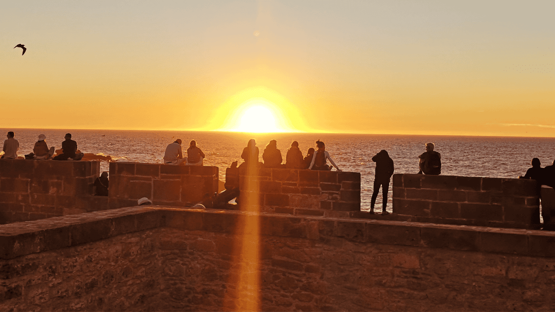Silhouetten einer WeRoad-Gruppenreise, die den Sonnenuntergang über dem Meer von einer Steinmauer aus beobachten.