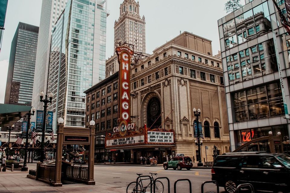 Una vista a nivel de calle del Teatro Chicago con su prominente letrero vertical, con un telón de fondo de rascacielos modernos y tráfico urbano.