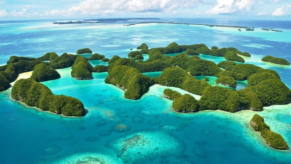 Vista aerea di un arcipelago tropicale con isole verdi lussureggianti sparse in un oceano turchese trasparente sotto un cielo nuvoloso.