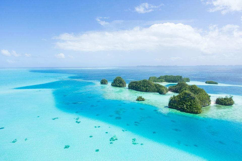 Una vista aerea di piccole isole rocciose coperte di vegetazione verde, sparse in un oceano turchese e blu intenso sotto un cielo parzialmente nuvoloso.